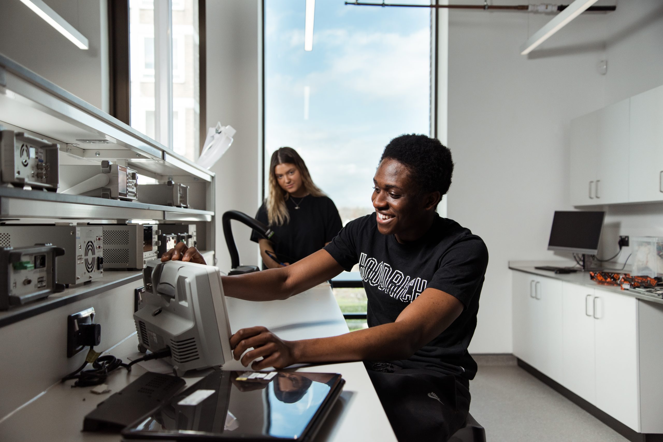 Two students, one standing and one sitting , working together in a monitor.