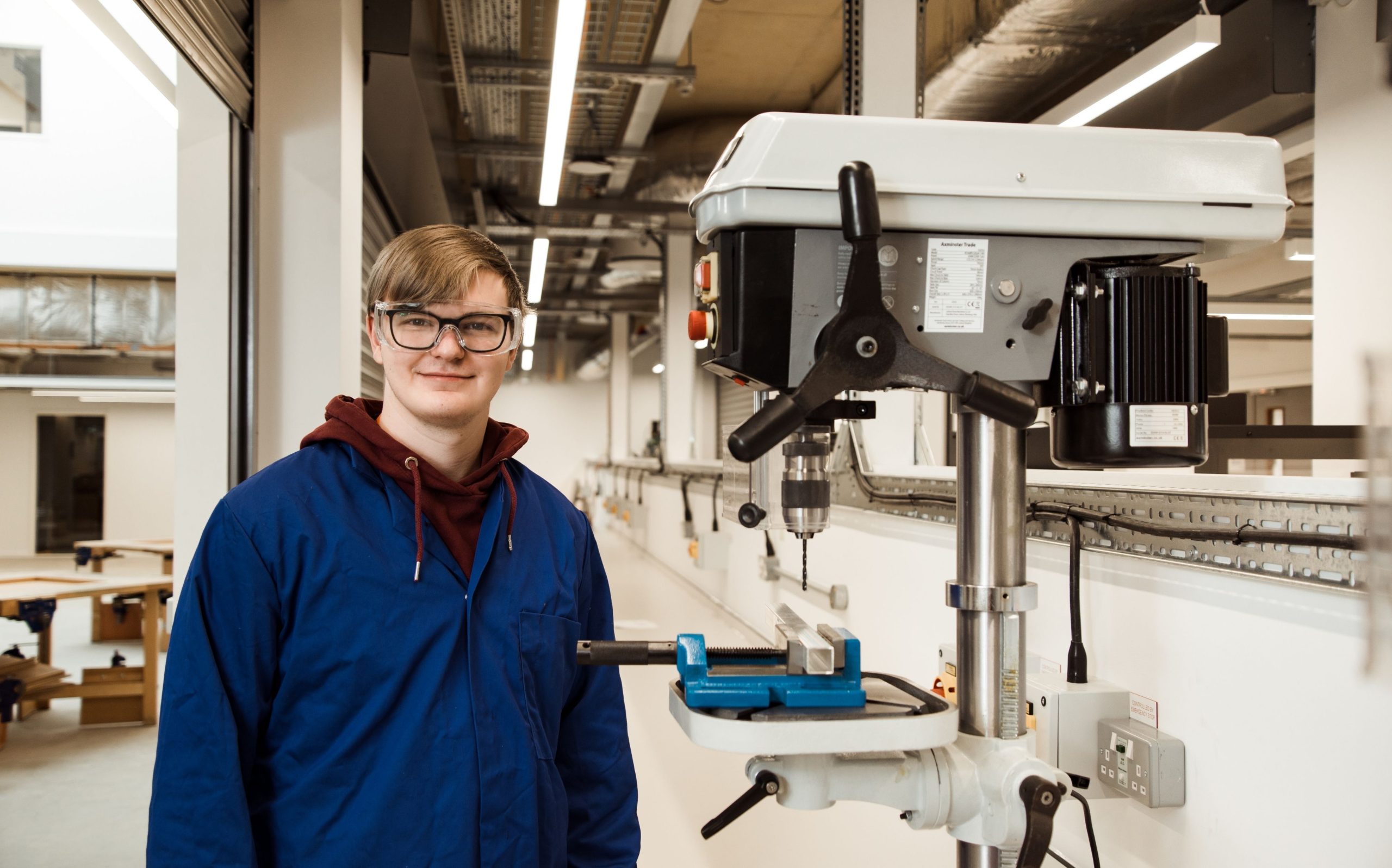 Student in navy blue lab coat standing next to specialist drill.
